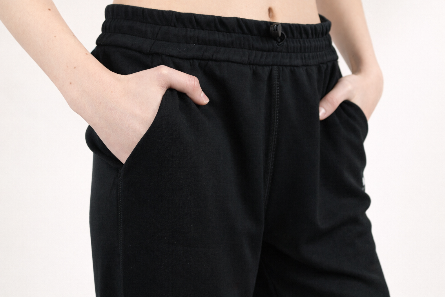 Person wearing black pants with hands in pockets on a white background