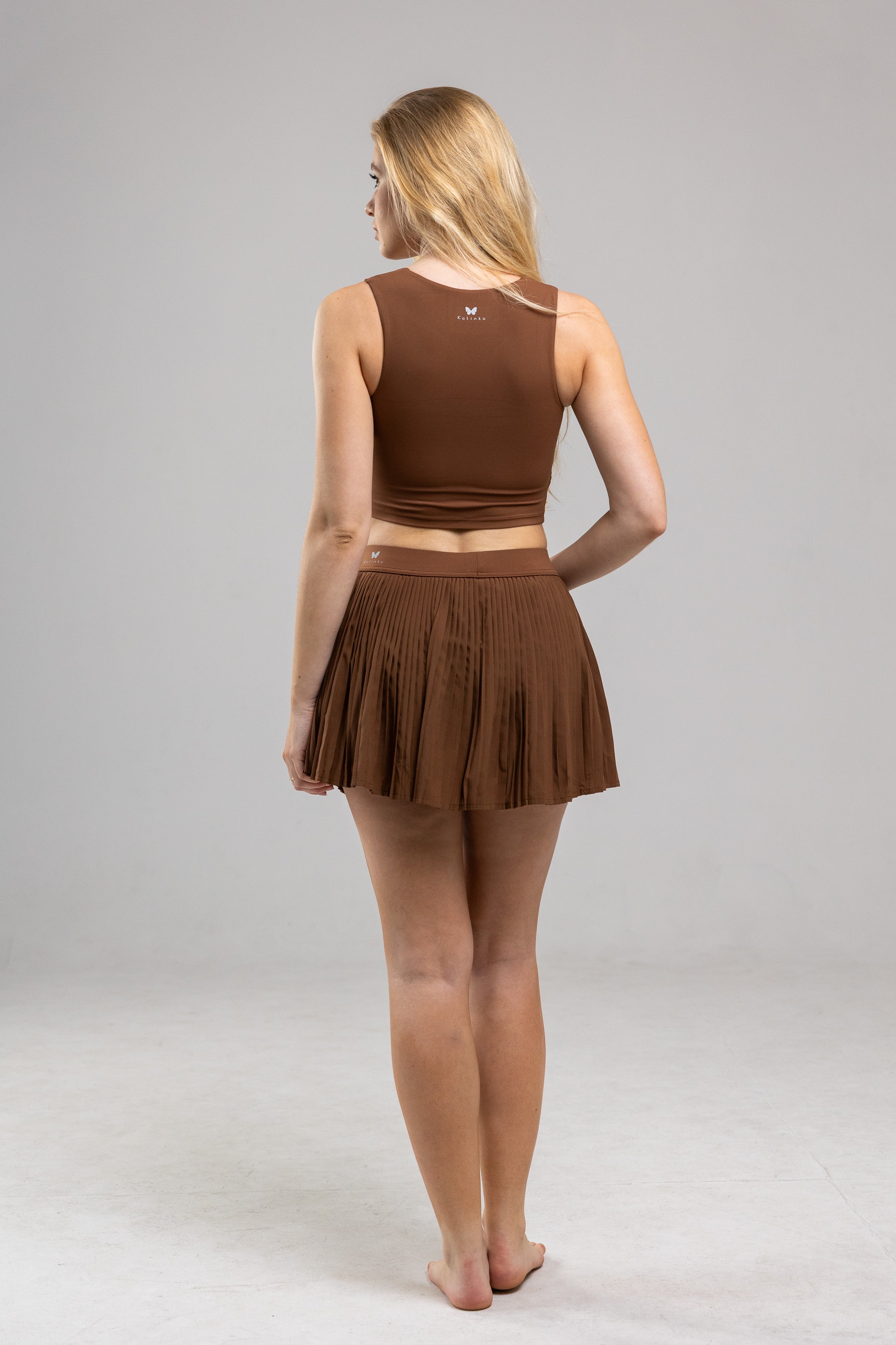 Woman wearing a brown crop top and skirt set on a gray background